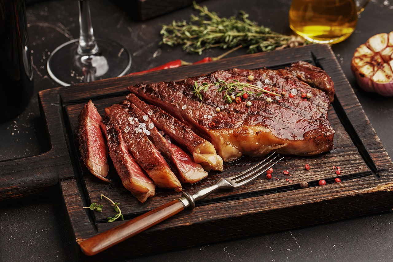 Medium-rare-sliced-grilled-striploin-beef-steak-served-on-wooden-board-with-vintage-fork